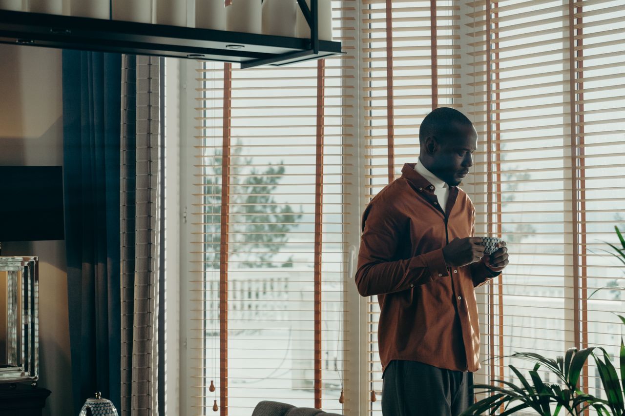 Man in casual attire sipping coffee by a window, serene interior setting.